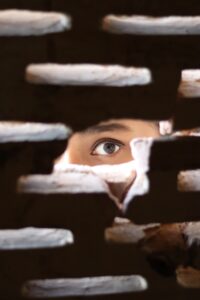 Person peering through crack in brick wall
