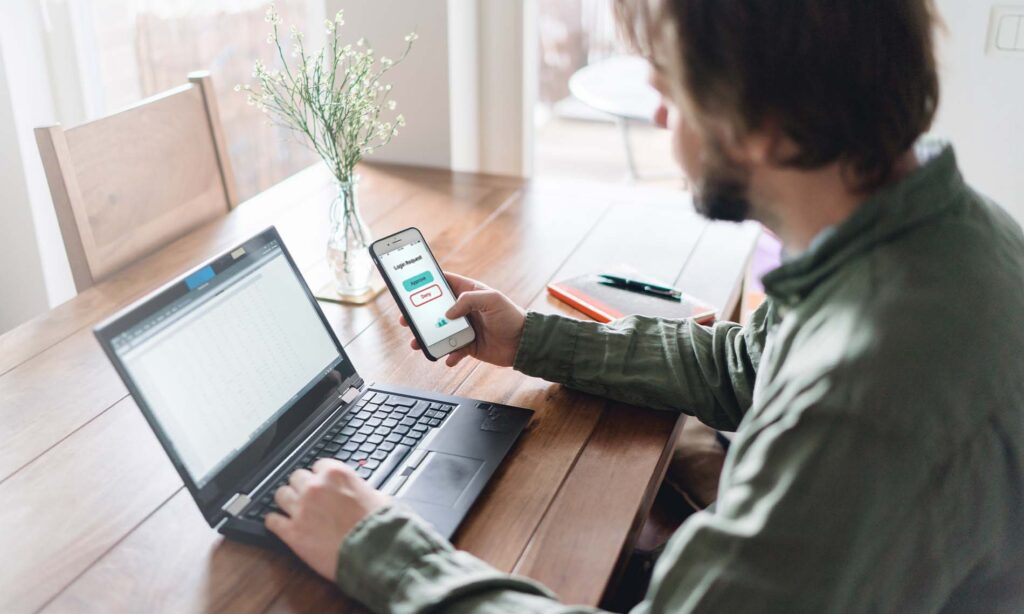 Man working on a laptop and logging into his phone using JumpCloud.