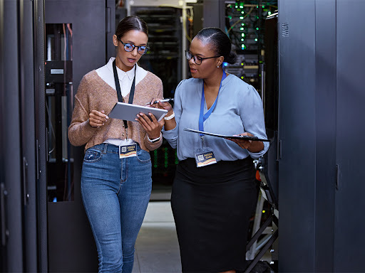 two women having a discussion over a tablet in a server room