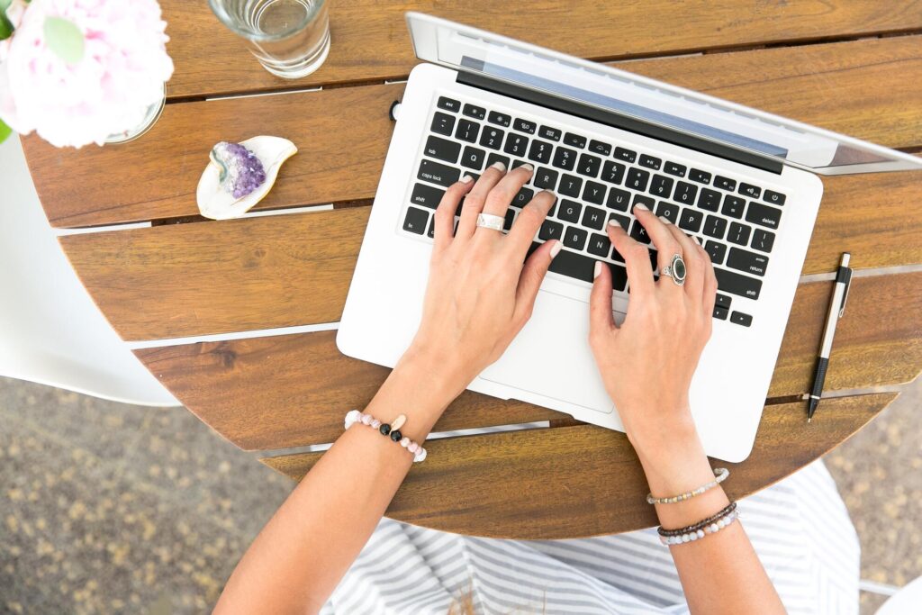 Woman in a striped dress working on a white laptop at a brown table.