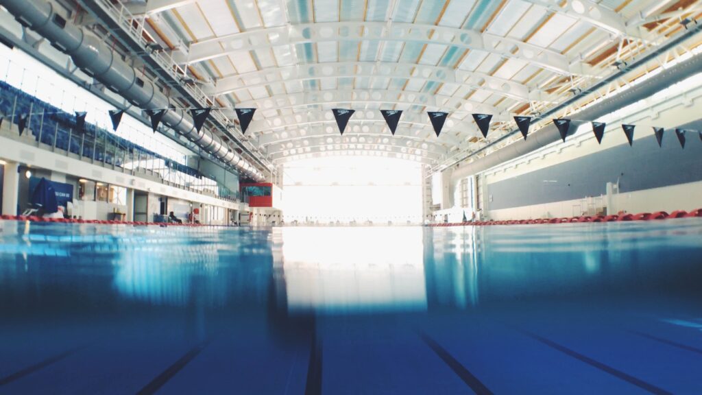 Large empty Olympic-sized swimming pool with blue triangular flags hanging across it.