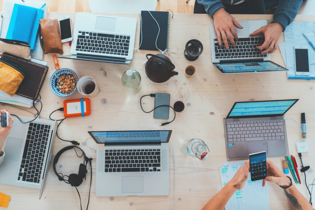 Laptops, phones, headphones, coffee, and notebooks on a table as a group brainstorms.