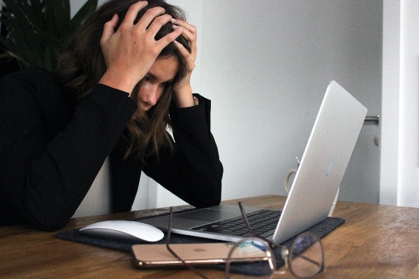 Woman working at a Macbook with her hands on her head in frustration.