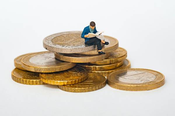 Small figure sitting on top of coins, illustrating how large certain IT costs can be.