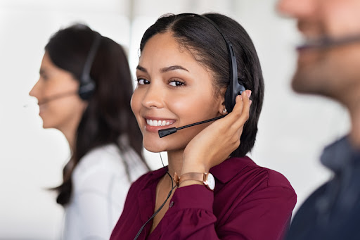 Smiling beautiful woman working in call center as telemarketing operator. Smiling customer support agent wearing headset at office, working while looking at camera. Middle eastern girl working as telephone operator with her colleagues.
