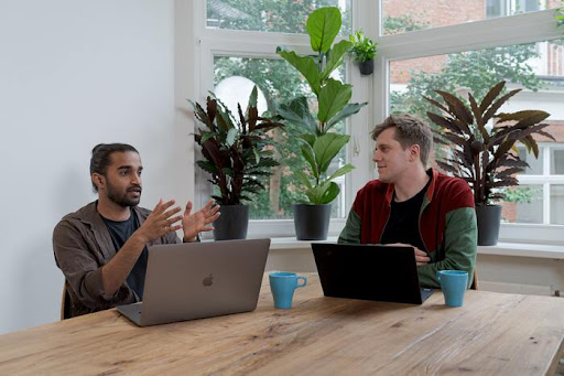 two men sitting at a table with their laptops having a meeting