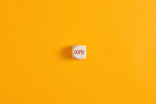 Oops sign on wooden cube over yellow background.