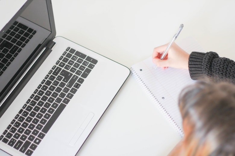 Person writing on paper with pen, next to a computer